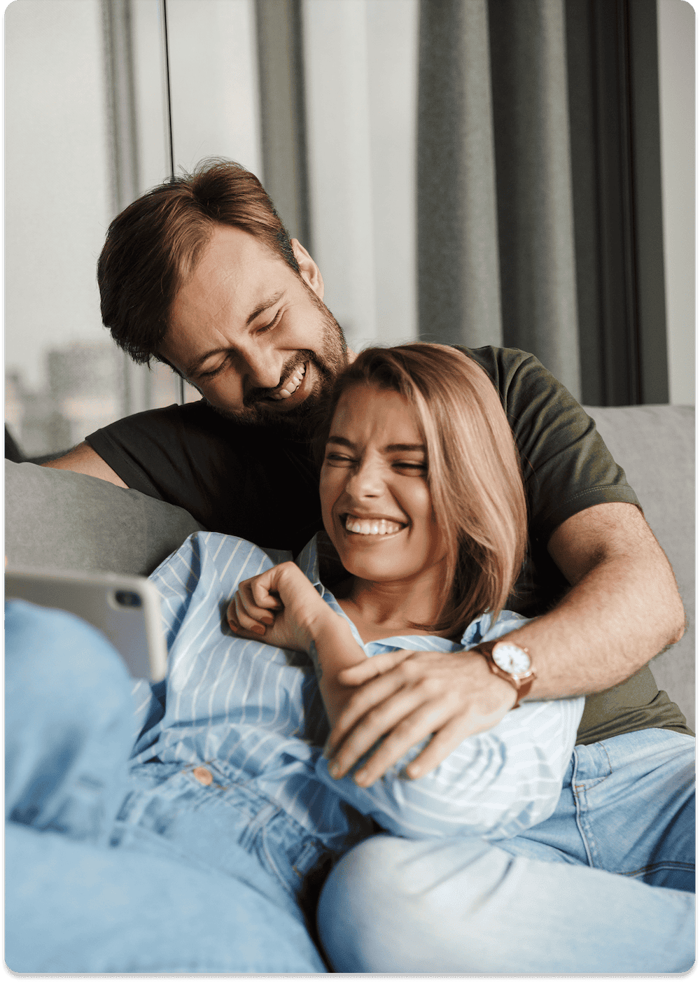 A man and a woman sit close together on a couch in Jacksonville, smiling and laughing while looking at a smartphone—perhaps searching for the best local air conditioning or HVAC services.